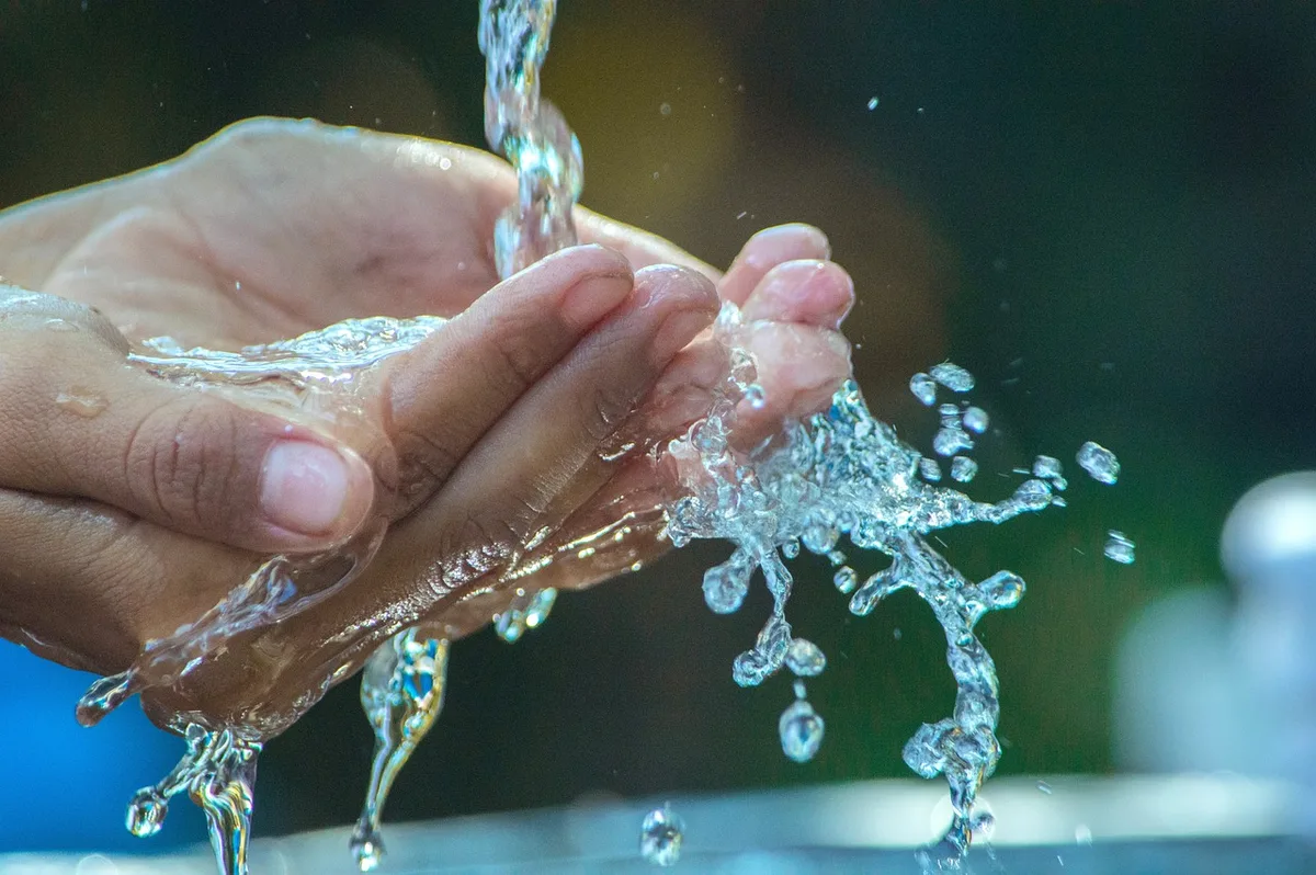 Verre d'eau posé sur une table en lumière du jour, mains en arrière-plan